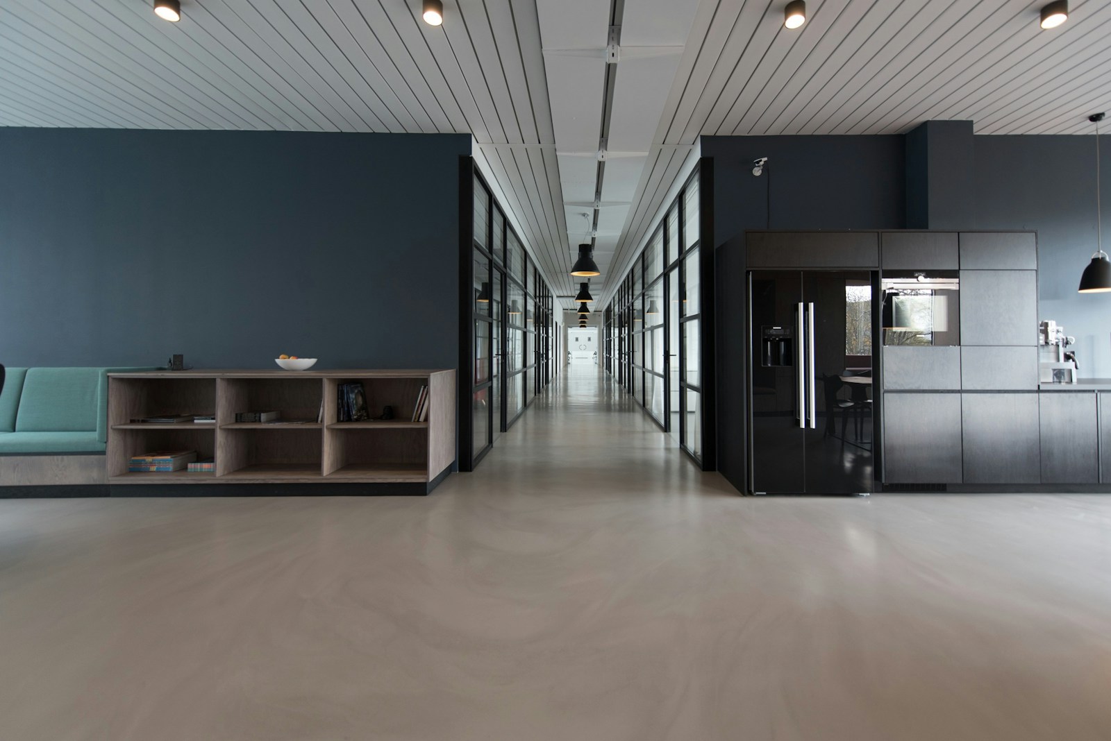 Modern workplace with a shared kitchenette, lounge seating and glass-lined corridor